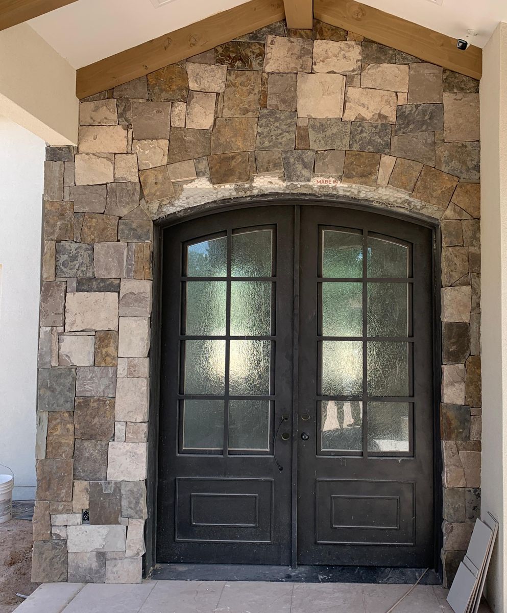 Arched iron French double doors with divided lites in a stone wall